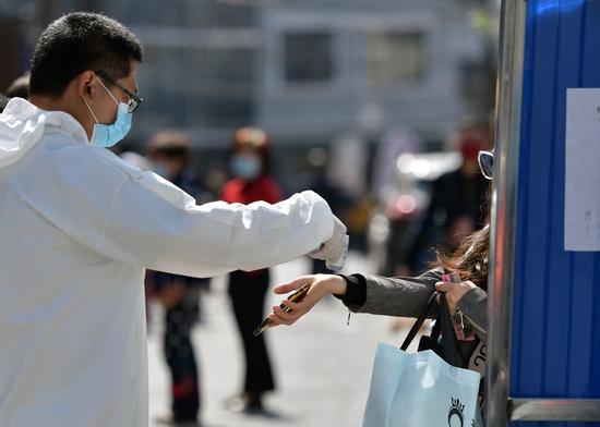 A staff member checks a resident's body temperature at the entrance of Chucai community in Wuchang District of Wuhan, central China's Hubei Province, April 15, 2020. (Xinhua/Li He)